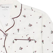 A close-up of a white long-sleeve pyjama top by Avery Row, featuring a delicate all-over print of small red berries with green leaves and dark burgundy piping along the collar, placket, and pocket.