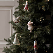Handmade knitted Christmas ornaments hanging on a decorated evergreen tree with warm string lights. The ornaments include a rocking horse, the sugar plum fairy, a nutcracker, a Christmas tree, and a small figure in colorful yarn.