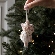 A hand holds a small handmade felt sugar plum fairy ornament with a white dress and gold embroidery, hanging against a dark green Christmas tree with warm string lights.