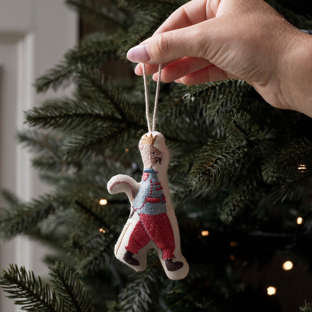 A hand hanging an embroidered Mouse King Christmas tree ornament.