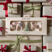 Avery Row Christmas tree decorations set of 5 in a cream-colored gift box, displayed on top of wrapped gift boxes with red ribbons and green satin bows.