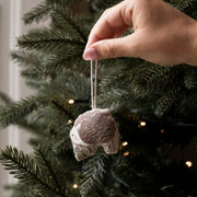 A hand hanging a small hedgehog ornament from a decorated Christmas tree. 