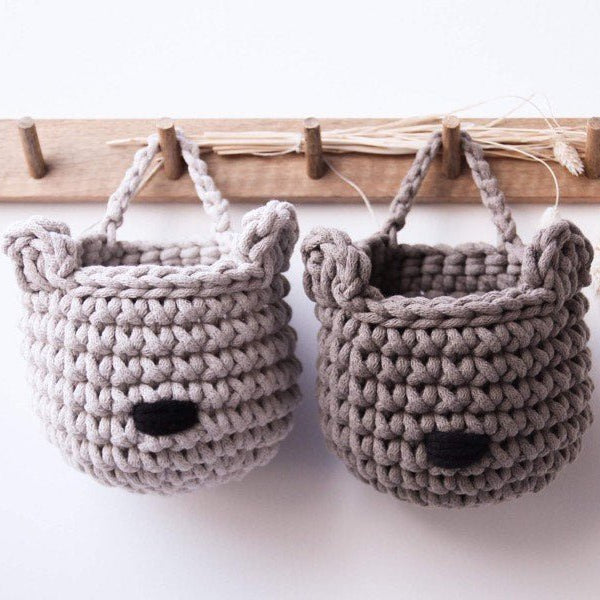 Two grey crochet bear shaped baskets hanging on a wooden rack.