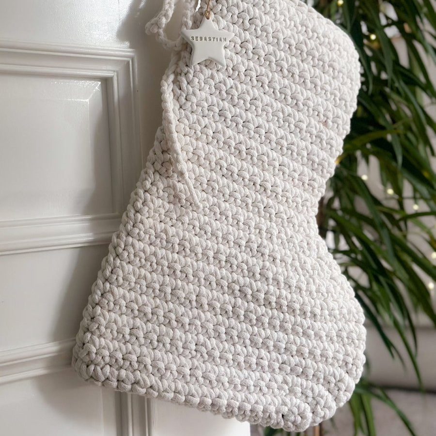 White knitted Christmas stocking hanging on a door handle with a plant in the background.