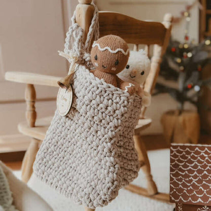Knitted gingerbread man in a crocheted Christmas stocking hanging on a wooden rocking chair and decorative items.