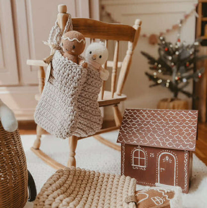 Children's room with wooden rocking chair, knitted Christmas stocking, and small gingerbread house.