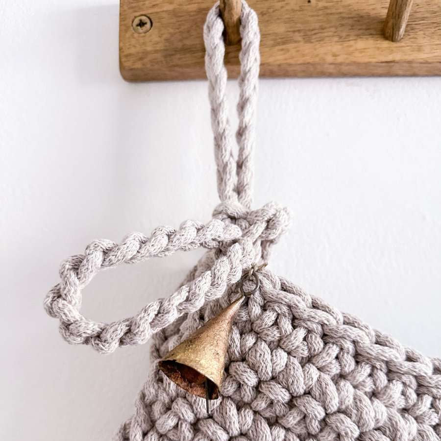 Crocheted hanging loop on Christmas stocking a wooden handle and metal bell on a white background