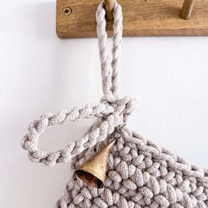 Crocheted hanging loop on Christmas stocking a wooden handle and metal bell on a white background