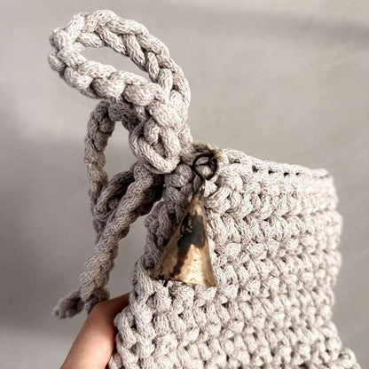 Hand holding an oatmeal crocheted Christmas stocking with a braided handle against a neutral background
