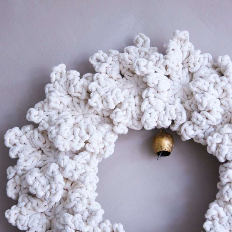 White textured wreath with a gold bell on a light grey background