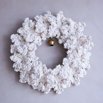 White crocheted wreath with a gold bell on a light gray background
