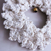 White crocheted wreath with a gold bell on a light grey background