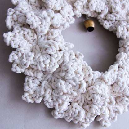 White crocheted wreath with a gold bell on a light grey background