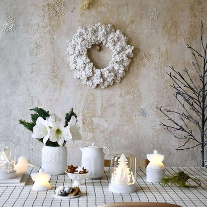 Decorative table setting with candles, flowers, and a wreath on a textured wall background.