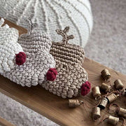 Crocheted reindeer Christmas stockings with red noses on a wooden surface next to small bells.