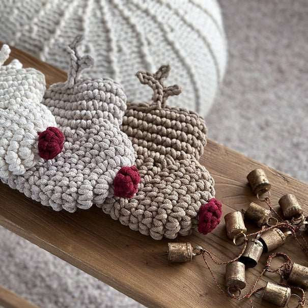 Crocheted reindeer Christmas stockings with red noses on a wooden surface next to small bells.