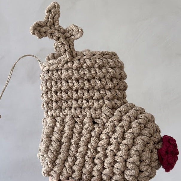 Handmade beige crocheted reindeer Christmas stocking with a red nose on a light grey background