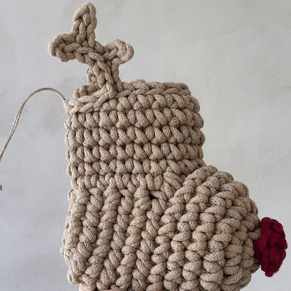Handmade beige crocheted reindeer Christmas stocking with a red nose on a light grey background
