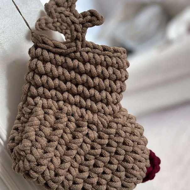 Brown knitted reindeer Christmas stocking with a red nose on a white surface
