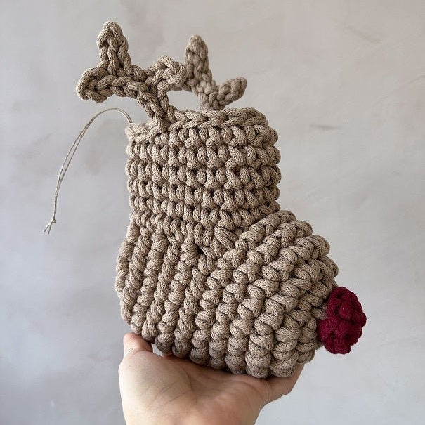 Handmade crochet reindeer Christmas stocking held by a hand against a plain background