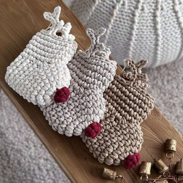 Three crocheted Christmas reindeer stockings with red noses and antlers on a wooden surface with small bells.