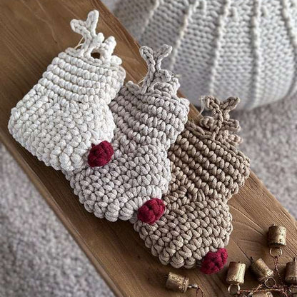 Three crocheted Christmas reindeer stockings with red noses and antlers on a wooden surface with small bells.