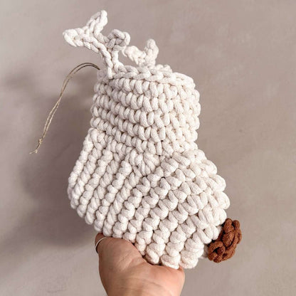 Handmade white crocheted stocking with antlers and a brown nose held by a hand against a neutral background