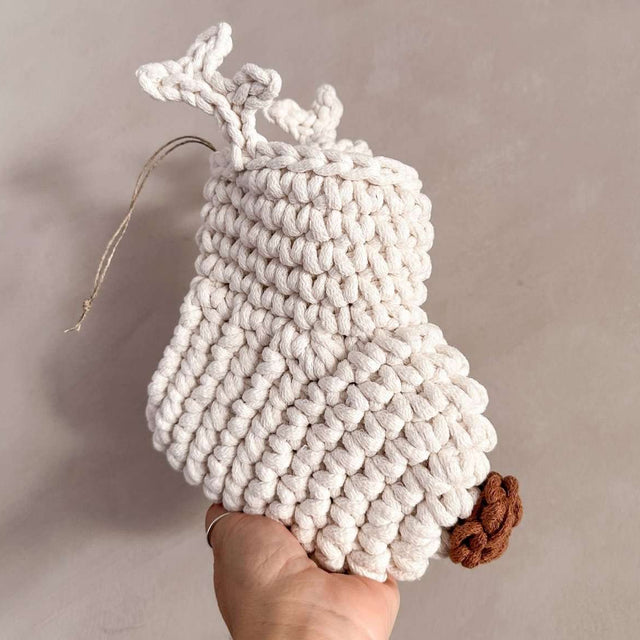Handmade white crocheted stocking with antlers and a brown nose held by a hand against a neutral background