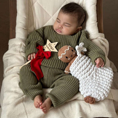 Baby in a green knitted outfit holding a knitted gingerbread man toy in a reindeer stocking