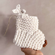 White crocheted Christmas stocking with antlers and a brown nose held by a hand against a neutral background
