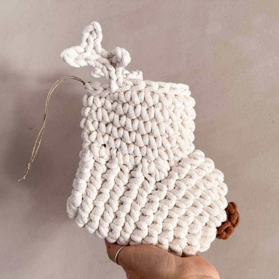 White crocheted Christmas stocking with antlers and a brown nose held by a hand against a neutral background