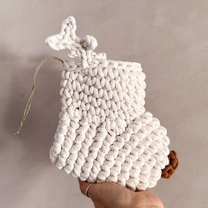 White crocheted Christmas stocking with antlers and a brown nose held by a hand against a neutral background