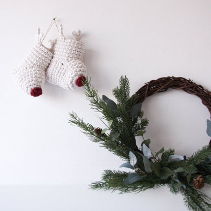 Decorative wreath with greenery and small white crocheted reindeer Christmas stockings on a plain background