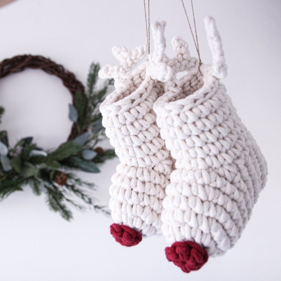 Knitted reindeer decorations with red noses on a white surface with a Christmas wreath in the background.
