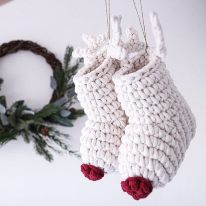 Knitted reindeer decorations with red noses on a white surface with a Christmas wreath in the background.