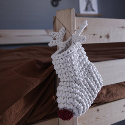 White knitted reindeer decoration on a wooden surface with a blurred background