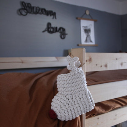 White crochet reindeer Christmas stocking decoration on a wooden bed with a blue wall and text in the background