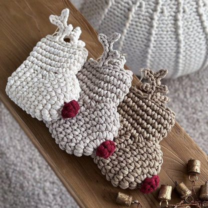 Three crocheted reindeer Christmas stockings with red noses on a wooden surface with small bells.