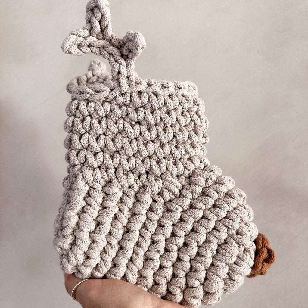 Knitted Christmas stocking with antlers and a brown nose held by a hand against a neutral background