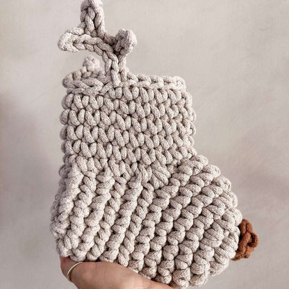 Knitted Christmas stocking with antlers and a brown nose held by a hand against a neutral background