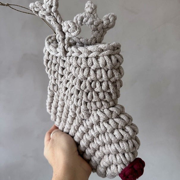 Handmade crocheted reindeer Christmas stocking with a red nose on a plain background