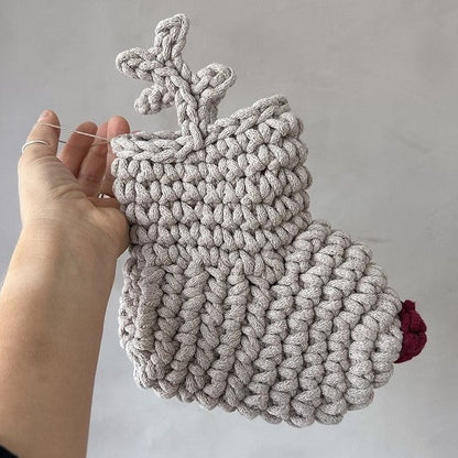 Hand holding a crocheted reindeer Christmas stocking with a red nose and antlers against a plain background