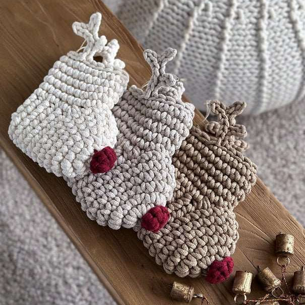 Three crocheted reindeer Christmas stockings with red noses on a wooden surface with small bells.