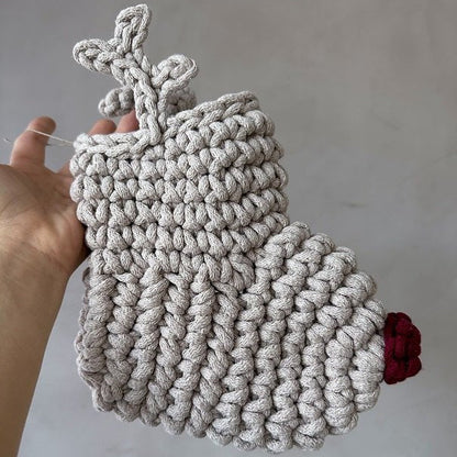 Handmade crocheted reindeer Christmas stocking with antlers and a red nose held against a plain background