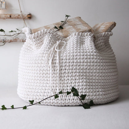 White crochet present sack on a white surface with green leaves.