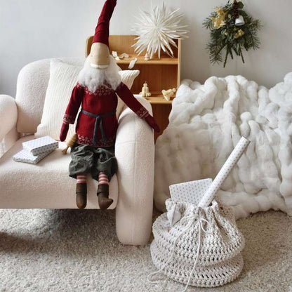 Decorative gnome on a white armchair with a crochet present sack and festive decorations in the background.