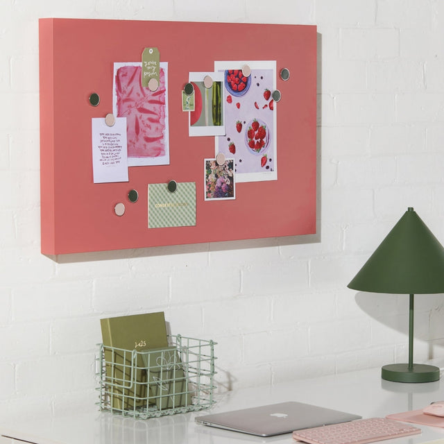 Pink magnetic bulletin board with pinned items on a white wall above a desk.