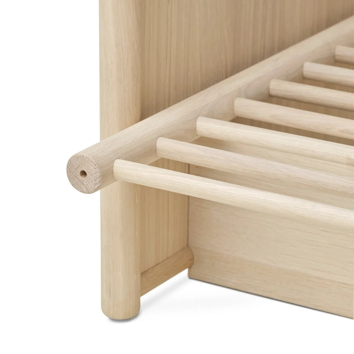 Close-up of a light natural wood bed frame corner with cylindrical support posts and slatted side rails on a white background.