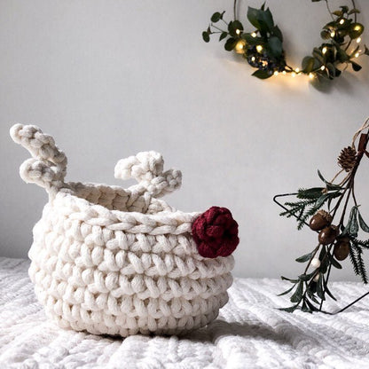 White crocheted reindeer basket with a red nose on a white surface, with decorative elements in the background.