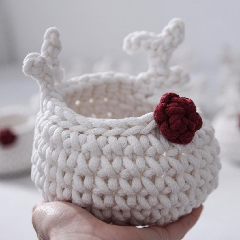 White crocheted reindeer basket with a red nose held by a hand 
